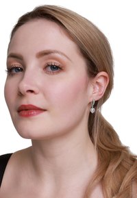 Zilveren oorbellen met een gebogen ontwerp bevatten een glanzende witte parel druppel, gedragen door een model met lichtbruin haar in een paardenstaart.