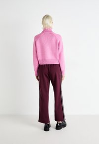 Cropped pink knit sweater with a high collar and ribbed hem paired with maroon wide-leg pants featuring side stripes and black platform shoes.