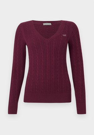 Kvinders langærmet kabelstrikket sweater i mørk burgundy med V-udskæring og lille broderet logo på brystet.