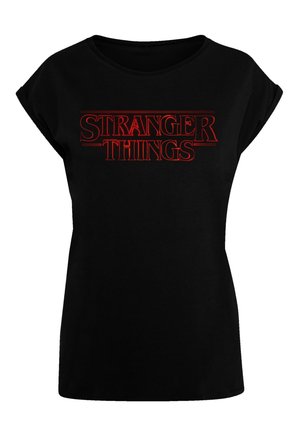Black short-sleeve T-shirt with a round neck featuring "STRANGER THINGS" in bold red capital letters across the front. Soft fabric texture.