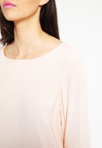 Haut à manches longues rose clair avec une texture lisse et un large col rond. Le tissu semble doux et tombe délicatement.