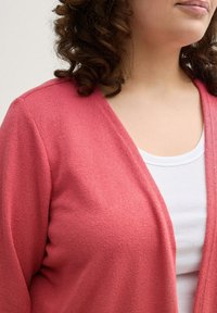 Korallenfarbener Cardigan mit strukturiertem Strickfinish, offener Vorderseite und tiefem V-Ausschnitt, kombiniert mit einem weißen gerippten Tanktop.