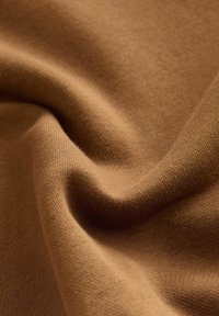 Tissu marron avec une texture lisse et douce, présentant un motif de tricot fin et un léger éclat, disposé en plis naturels.