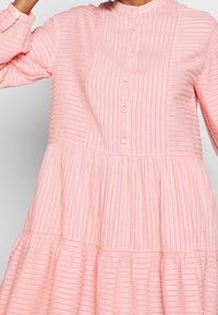 Abito rosa a righe con scollatura rotonda, chiusure con bottoni e strati arricciati. Realizzato in tessuto leggero con una finitura testurizzata.