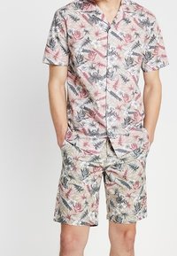 Camisa de manga corta floral y pantalones cortos a juego en beige claro con patrones botánicos en rosa, verde y gris. Tejido ligero, ajuste casual.