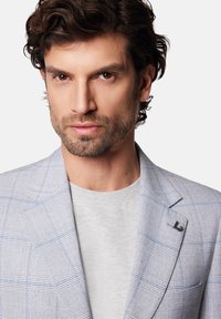 Jasnoszary marynarka w kratę z niebieskimi akcentami, połączona z szarym T-shirtem. Zawiera charakterystyczną przypinkę na klapie.