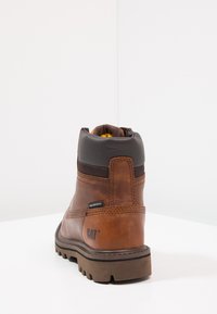 Bota impermeable de cuero marrón con un cuello acolchado negro y suela marrón, con acentos de costura y un logotipo de CAT en el lado.