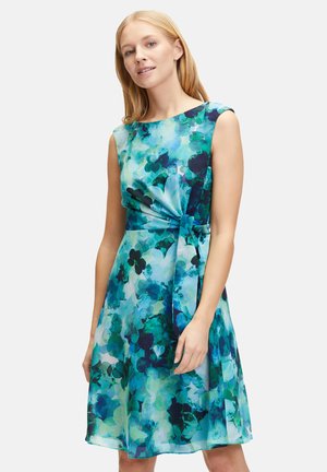 Blumenkleid mit einem Knoten-Detail an der Taille. Der Stoff zeigt eine Mischung aus Blau- und Grüntönen in einem Aquarellmuster. Ärmellos mit rundem Ausschnitt.