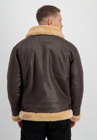 Chaqueta de cuero marrón con un suave cuello y puños de borreguillo color beige. Superficie texturizada, corte relajado y detalle de cierre oculto en el dobladillo.