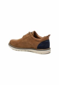 Zapato de ante marrón con un acento azul marino en el talón, presenta una puntera redondeada, diseño de cordones y una suela de goma blanca.