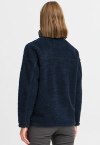 Mørkeblå fleecejakke med teksturert, fluffy design, høy krage og løs passform. Har lange ermer og buet kant.