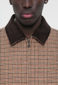 Barna kockás dzseki barna kordbársony gallérral, elöl cipzárral és texturált anyaggal. Közeli kép, elölnézet.