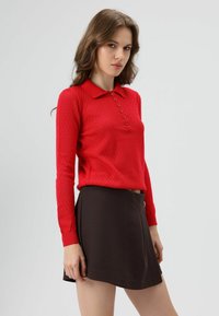 Rode gebreide poloshirt met lange mouwen, een kraag en knopen aan de voorkant, gecombineerd met een bruine uitlopende rok, gladde textuur en eenvoudig ontwerp.