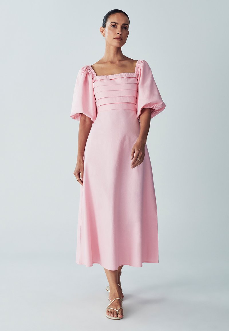 Roze, vloeiende midi-jurk met een vierkante halslijn, pompomenmouwen en geplooide details op het lijfje; gemaakt van lichtgewicht stof.