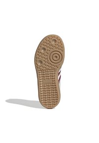 Podešev tenisky Adidas v béžovém gumovém provedení s texturovaným diamantovým vzorem, obsahující kruhový emblém a logo Adidas, vykazuje známky opotřebení.