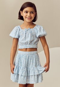 Világoskék, virágmintás két részes öltözék, fodros ujjú, rövid top és bővülő, réteges szoknya. Pamut anyag.