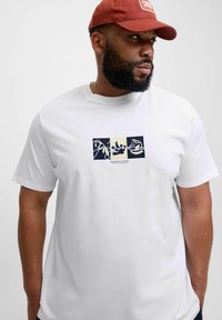 Hvid bomulds T-shirt med et grafisk print, der viser et mørkeblåt og beige design. Rund halsudskæring, korte ærmer, glat tekstur.