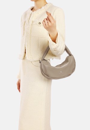 Borsa a mano in pelle beige con una silhouette curva e una superficie liscia, tenuta da una persona che indossa una giacca crema con texture.