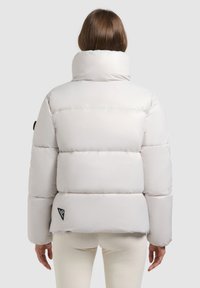 Hvid pufferjakke med høj krave, karakteriseret ved et quiltet design og en tætsiddende pasform. Har et sort logo-patch ved kanten.