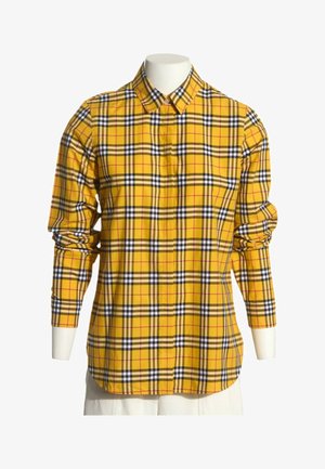 Gul langærmet skjorte med knapper og tern i sort, hvid og rød på en hvid mannequin-figur.