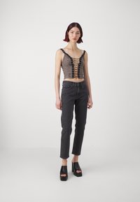 Black cropped top with lace-up front and silver eyelets, paired with high-waisted black jeans. Model wears chunky black platform sandals.