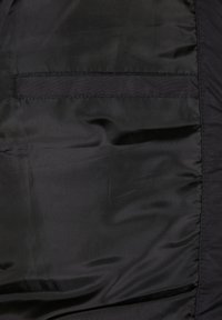 Tejido de nylon negro con una textura suave, que presenta una costura de bolsillo horizontal y detalles fruncidos a lo largo de un borde.
