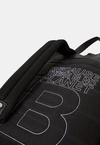 Zaino nero con texture trapuntata, con testo bianco che recita "PERCHÉ NON C'È UN PIANETA" e una grande lettera "B". Spallacci a rete.