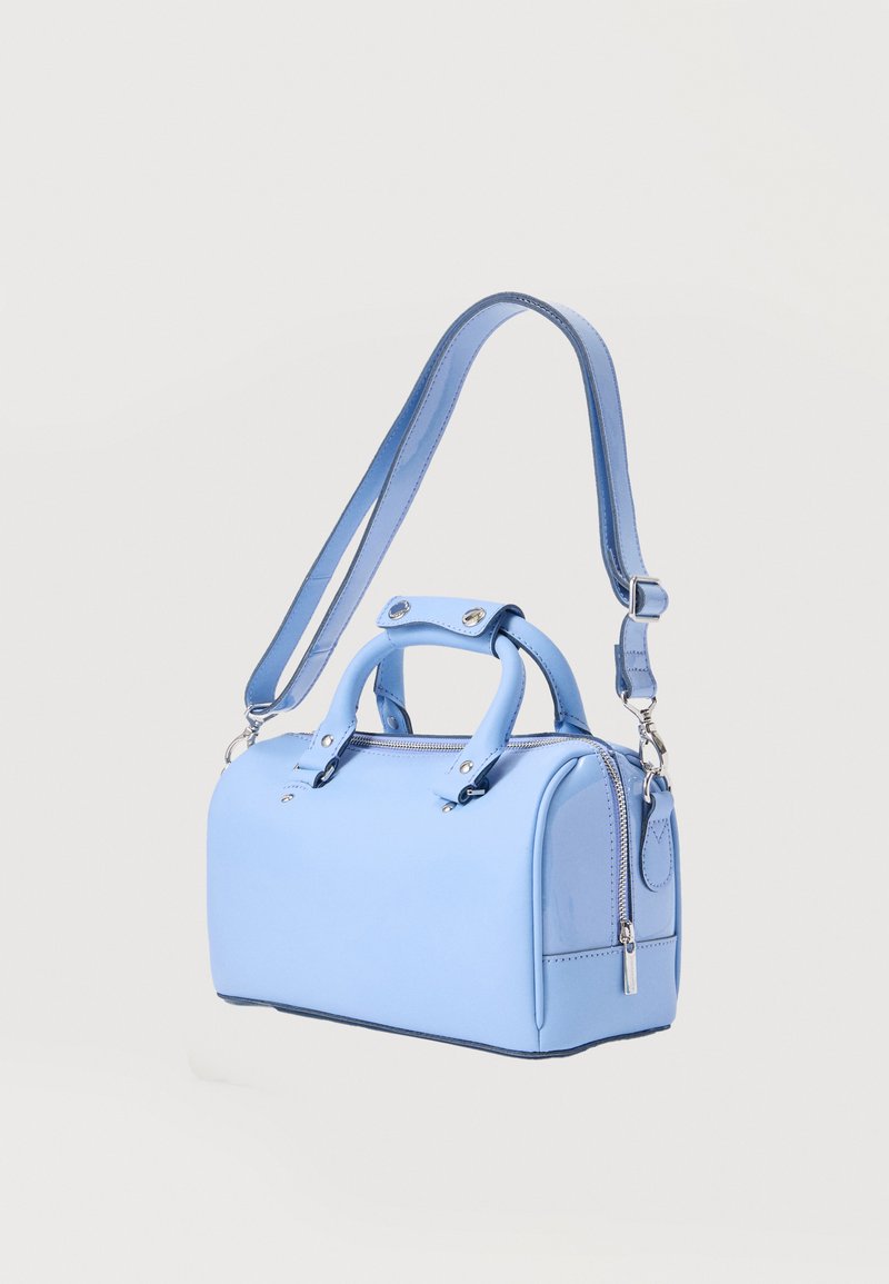 Hellblaue Lederhandtasche mit doppelten Griffen, abnehmbarem, verstellbarem Schulterriemen und Reißverschluss oben vor einfarbigem Hintergrund.