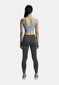 Soutien-gorge de sport bleu clair avec un dos en forme de scoop, associé à un legging vert foncé avec une texture lisse et des détails de couture subtils. Chaussures de sport incluses.