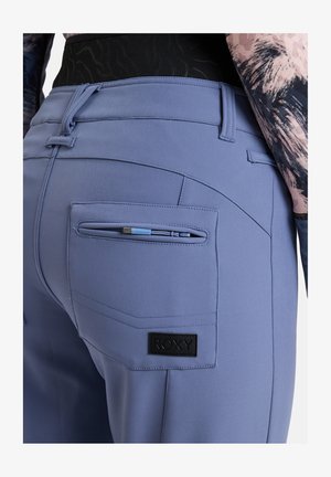 Pantaloni Roxy da donna in morbido tessuto lavanda, con tasca posteriore con zip, patch logo nero e design su misura con cuciture dettagliate.