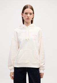 Felpa color crema con tasca frontale, cappuccio con coulisse e logo discreto in rosa. Tessuto morbido, vestibilità comoda e polsini a coste.