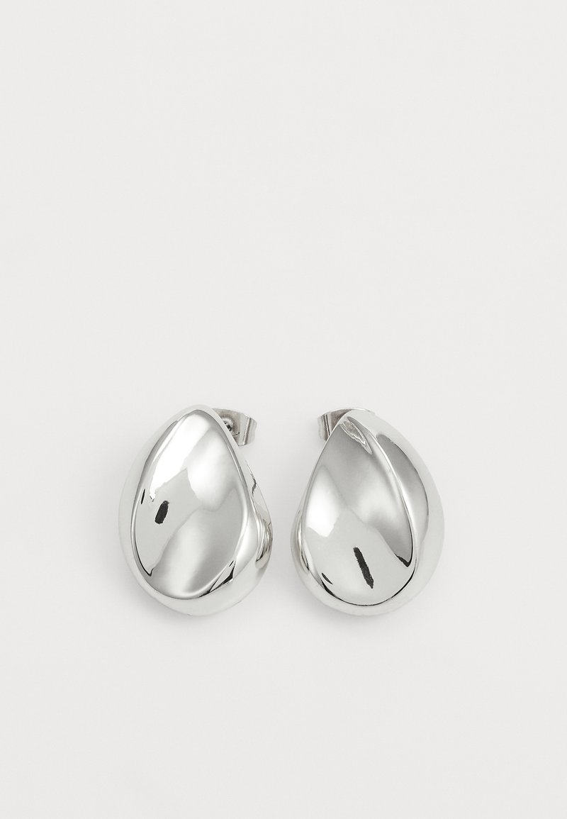 Boucles d'oreilles argentées à clip, de forme goutte d'eau, présentant une surface lisse et réfléchissante ainsi qu'un design subtilement courbé pour une dimension supplémentaire.