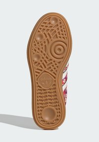 Suela de zapato Adidas de color goma con un diseño de tracción circular y de patrón, logo de Adidas visible, y parte de la parte superior del zapato con un patrón floral.