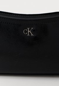 Μαύρο, λαμπερό δερμάτινο αντικείμενο με ασημένια λεπτομέρεια λογότυπου "cK" στο κέντρο της επιφάνειάς του.