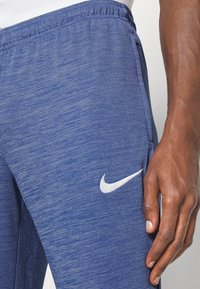 Blauwe sportbroek van gestructureerd materiaal, met een elastische tailleband en een wit Nike-logo aan de zijkant.