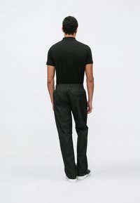 Fekete galléros póló fekete, könnyű, elasztikus derékpánttal rendelkező nadrággal párosítva. Az alacsony profilú tornacipők tökéletesen kiegészítik a monokróm megjelenést.