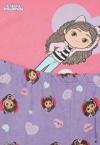 Světle růžový bavlněný top s ilustrací postavy v pruhované mikině. Fialové dno s opakovanými vzory srdcí.