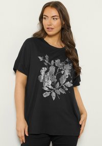 Zwarte oversized t-shirt met korte mouwen, voorzien van een zilveren botanische afdruk op de voorkant. Zacht katoenmateriaal, relaxte pasvorm.
