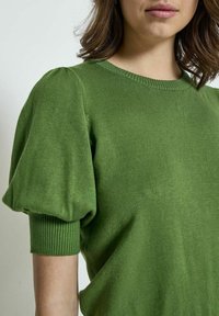 Maglione verde a maglia con maniche corte a sbuffo, scollo rotondo e una finitura morbida e testurizzata. I polsini a coste arricchiscono il design.