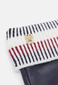 Strikket taske med et hvidt, rødt og marineblåt stribet mønster. Har en guld logo detalje. Fremstillet af uld og læder, med en blød tekstur.