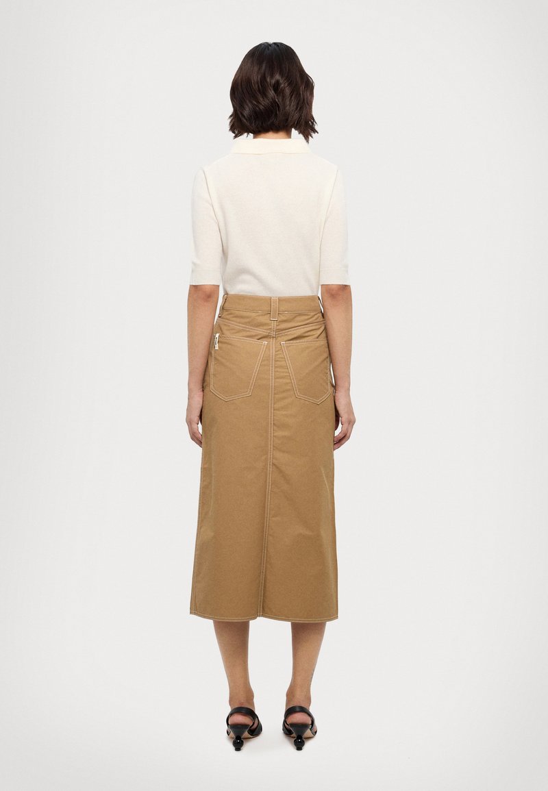 Falda de algodón beige con longitud a media pantorrilla, que presenta dos bolsillos en la parte trasera, costuras visibles y un corte recto. Detalle sencillo en la cintura.