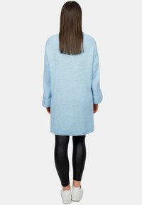 Maglione oversize lavorato a maglia di colore blu chiaro, con maniche lunghe, abbinato a leggings in pelle nera e sneakers bianche, visto da dietro.