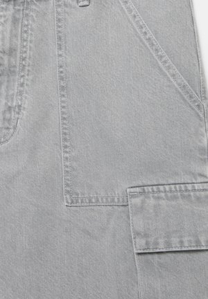 Nahaufnahme von hellgrauem Denimstoff mit detaillierter Naht und einer Klappentasche an der Seite eines Kleidungsstücks.