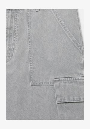 Nahaufnahme von hellgrauem Denimstoff mit detaillierter Naht und einer Klappentasche an der Seite eines Kleidungsstücks.