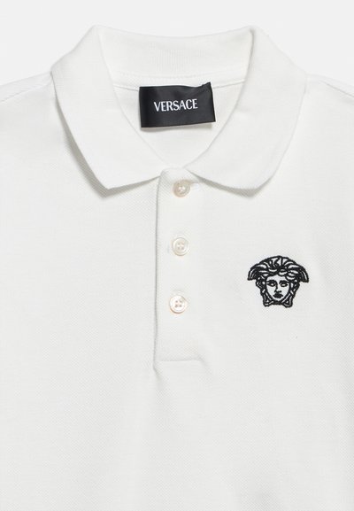 Λευκό πόλο πουκάμισο με τρία κουμπιά, μαύρο κεντημένο λογότυπο κεφαλής Μέδουσας στο στήθος και μαύρη ετικέτα Versace μέσα στη γιακά.