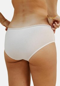 Shorty en coton blanc avec une ceinture élastique à bords festonnés et un design lisse et simple, offrant un ajustement serré et sans motifs visibles.
