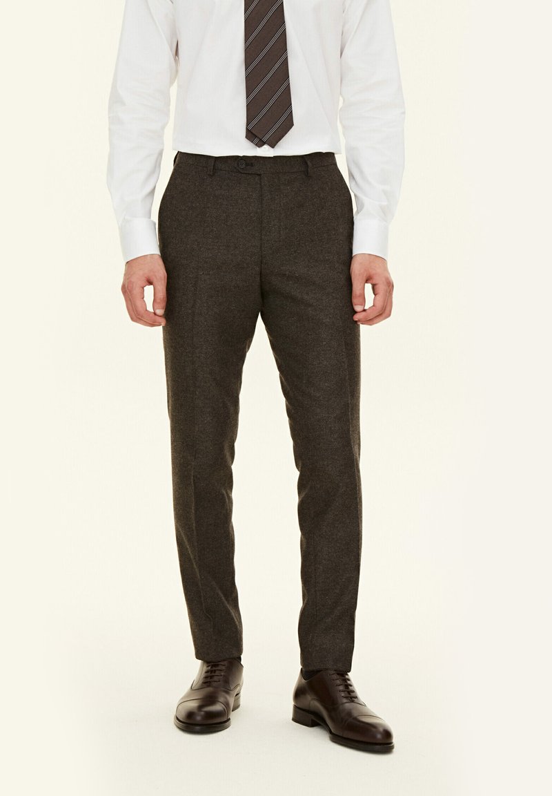 Pantaloni grigi su misura realizzati in un tessuto testurizzato, con un design aderente e un frontale piatto, abbinati a scarpe eleganti marroni lucide.