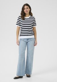 Haut à manches courtes rayé noir et blanc, associé à un jean large bleu clair et des ballerines noires. Tissu lisse et coupe décontractée.