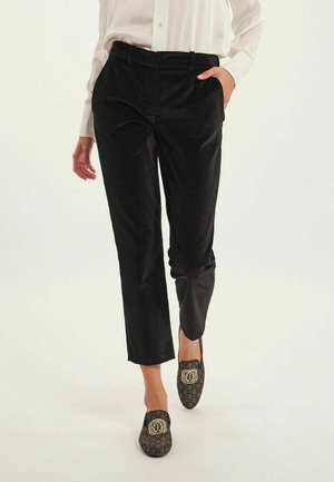 Pantalon en corduroy noir avec une coupe slim, doté de poches latérales peu profondes et d'une texture lisse, associé à des mocassins noirs à motif.