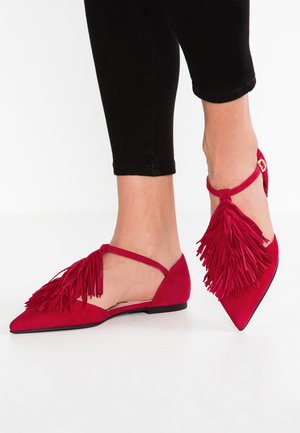 Røde ruskinds flade sko med spids tå, sideskæringer og fremtrædende frynsedetalje foran. Inkluderer ankelstrop med gulddetaljer.